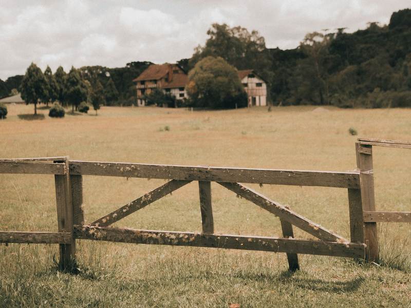 A wooden farm gate in a pasture with a farmhouse in the distance